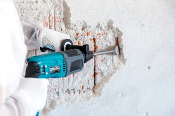 Worker removes plaster from a brick wall with a perforator