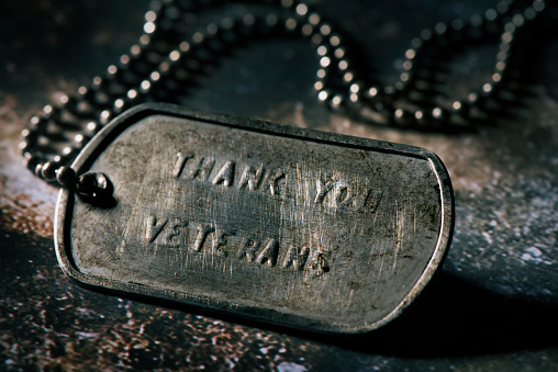 closeup of a rusty dog tag with the text thank you veterans written in it, on a rustic gray surface