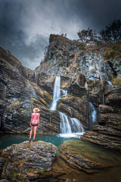 istock Woman stands in awe at waterfall tumbling over cliffs 1185639265