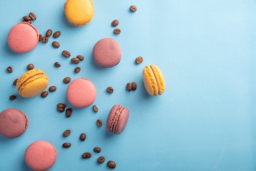 Colorful French or Italian macaron stack and coffee bean on blue table with copy space for background. Top view