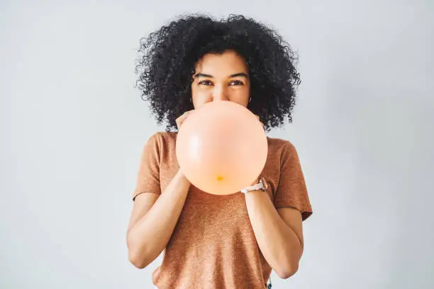 Shot of a young woman blowing up a balloon against a grey background