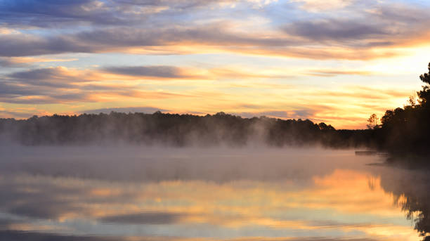 istock Layer of bright wispy clouds over steaming forest lake with pier at sunrise 1185642033