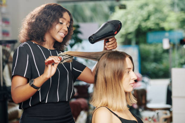 Hairdresser working in beauty salon Positive young Black hairdresser enjoying working in beauty salon and blowdrying hair of client blow drying stock pictures, royalty-free photos & images