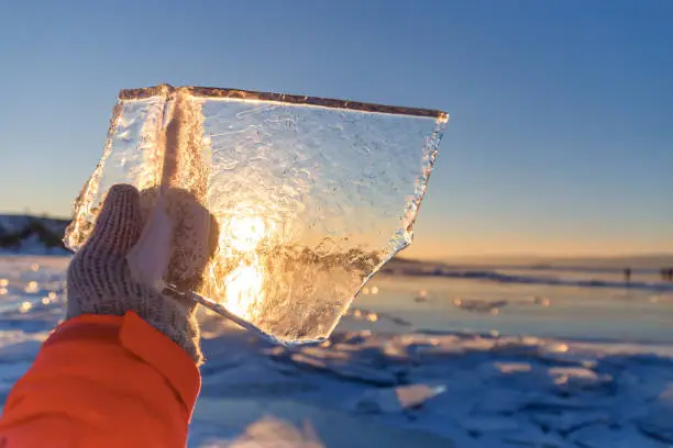 Winter landscape,Sun shines through clear ice chunk in a hand, Lake Baikal, Siberia, Russia.