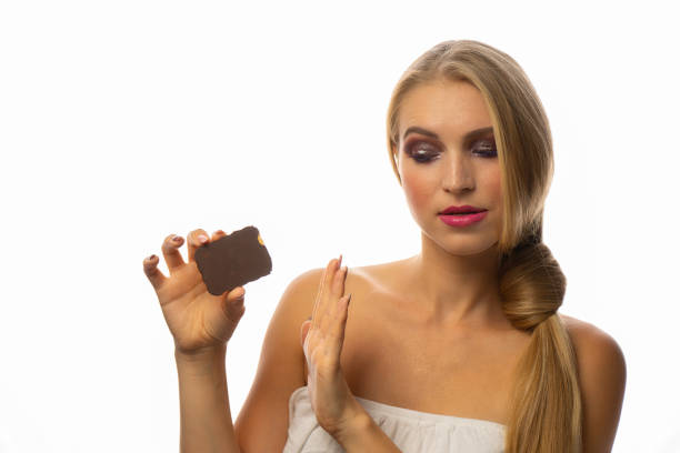 Young woman eating chocolate cookie ,with shame for mistake. Over isolated background