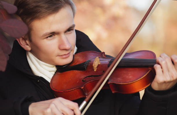 istock face profile of a young elegant man playing the violin on autumn nature backgroung, a boy with a bowed orchestra instrument makes a concert, concept of classical music, hobby and art 1185649512