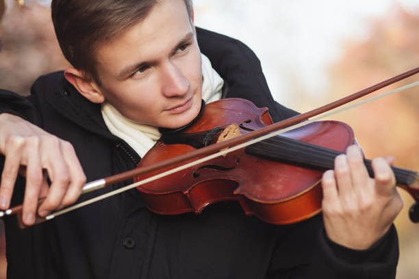 istock face profile of a young elegant man playing the violin on autumn nature backgroung, a boy with a bowed orchestra instrument makes a concert, concept of classical music, hobby and art 1185649542