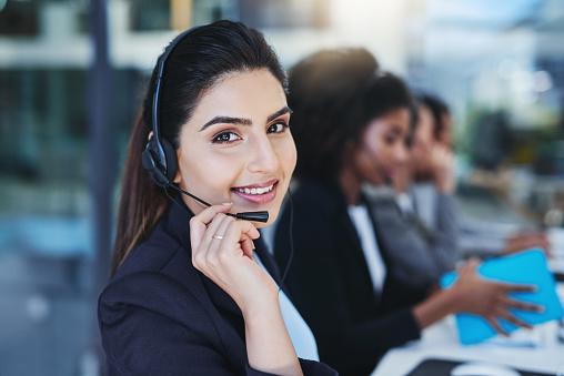 Cropped portrait of an attractive young businesswoman sitting in the office with her coworkers and wearing a headset