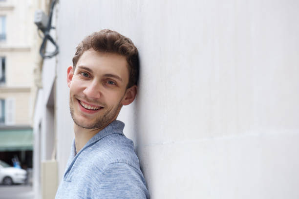 istock young man leaning against wall and smiling 1185650738