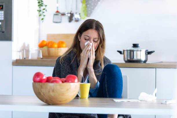 istock Illness young woman sneezing in a tissue while sitting in the kitchen at home. 1185652993
