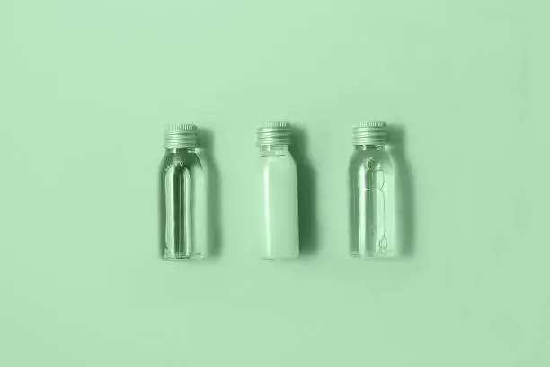 Flat lay of three small mockup bottles with spa cosmetic products in trendy mint color. Women beauty and beauty salon cosmetics concept. Eco concept.