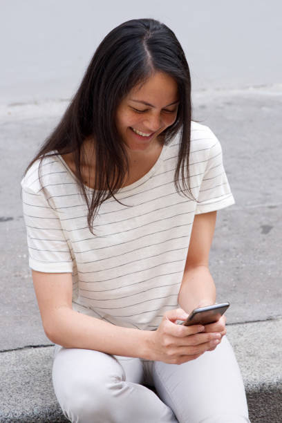 istock smiling young asian woman using cellphone outdoors 1185657370