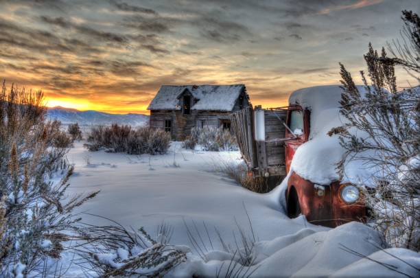 Rustic log barn has wooden roof and is in disrepair.  Field behind barn rolls across the distance to the mountains of Paradise Valley, Montana.