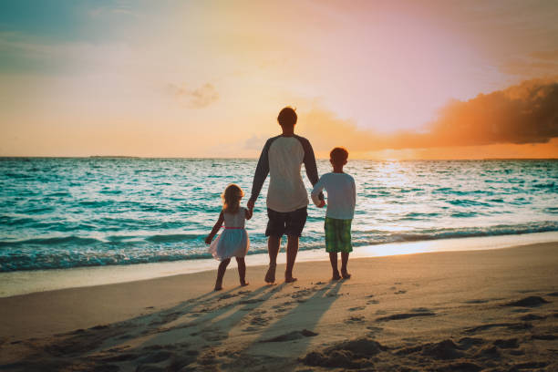 istock father with son and daughter walking on beach at sunset 1185665852