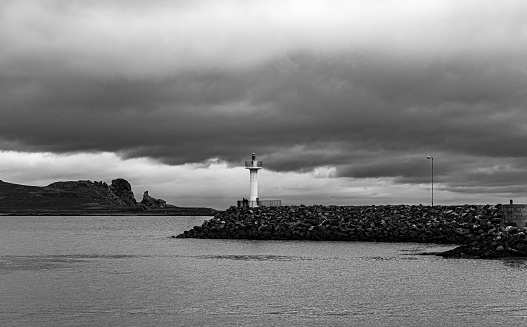 Howth harbour lighthouse with sea and rocks in view - Black & White