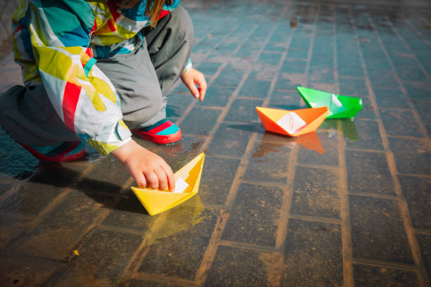 istock child playing with paper boats in water puddle 1185669366