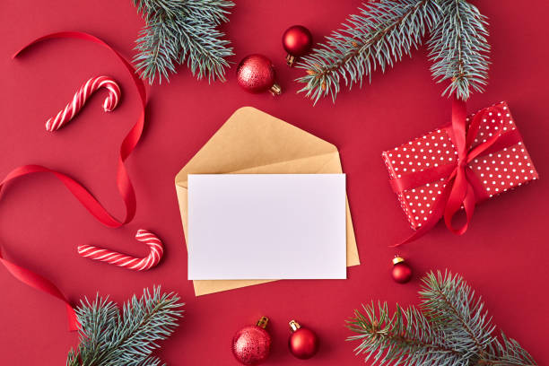 Mockup white greeting card and envelope with red christmas balls, spruce branches and gift box on a red background