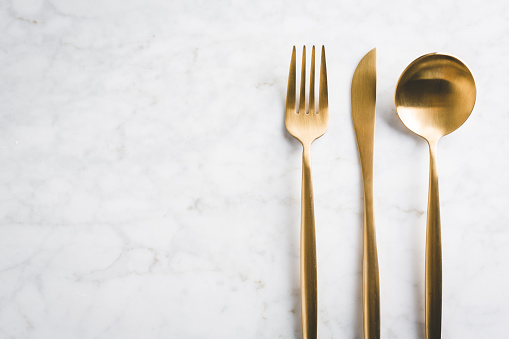 Beautiful gold cutlery - fork, knife, spoon on marble background. Horizontal.