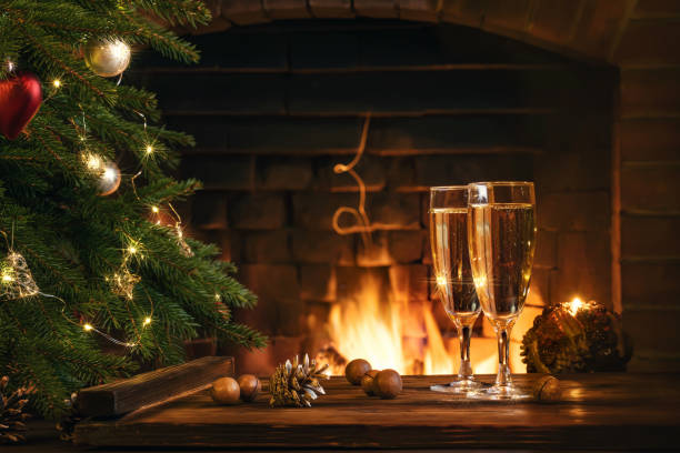 Christmas composition - Two glasses with champagne on a wooden table near a Christmas tree in a room with a burning fireplace Christmas composition - Two glasses with champagne on a wooden table near a Christmas tree in a room with a burning fireplace. carbonated photos stock pictures, royalty-free photos & images