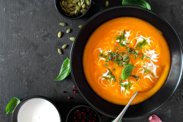 istock Pumpkin and carrots soup with cream and basil on dark background. 1185674903