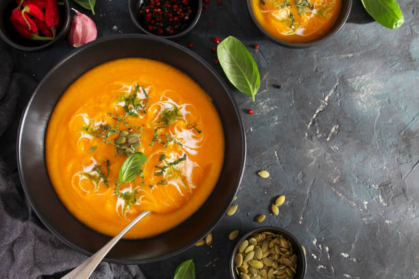 istock Pumpkin and carrots soup with cream and basil on dark background. 1185676015