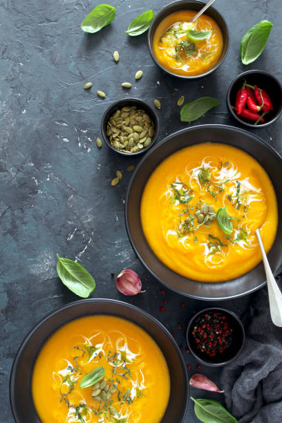 istock Pumpkin and carrots soup with cream and basil on dark background. 1185676113