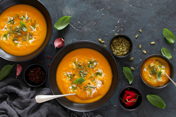 istock Pumpkin and carrots soup with cream and basil on dark background. 1185676123