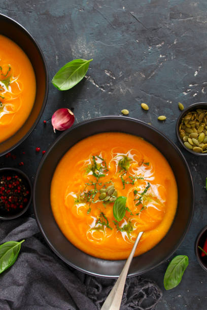 istock Pumpkin and carrots soup with cream and basil on dark background. 1185676126