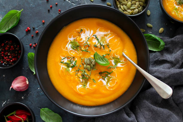 istock Pumpkin and carrots soup with cream and basil on dark background. 1185676807