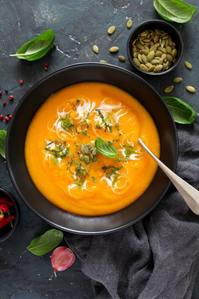 istock Pumpkin and carrots soup with cream and basil on dark background. 1185677692