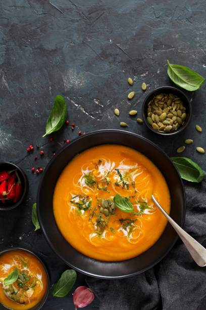 istock Pumpkin and carrots soup with cream and basil on dark background. 1185677799