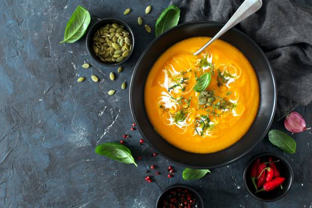istock Pumpkin and carrots soup with cream and basil on dark background. 1185677800
