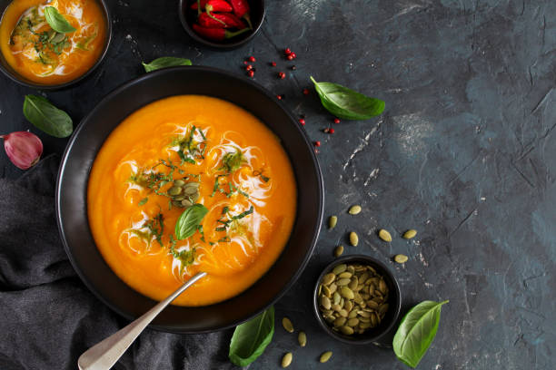 istock Pumpkin and carrots soup with cream and basil on dark background. 1185677804