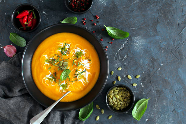 istock Pumpkin and carrots soup with cream and basil on dark background. 1185677920
