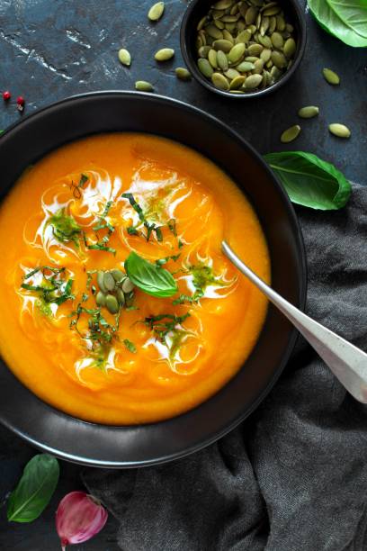 istock Pumpkin and carrots soup with cream and basil on dark background. 1185678140