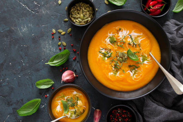 istock Pumpkin and carrots soup with cream and basil on dark background. 1185678407