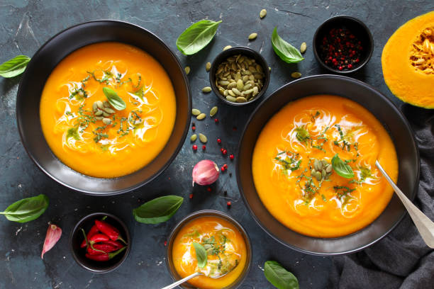 istock Pumpkin and carrots soup with cream and basil on dark background. 1185678693