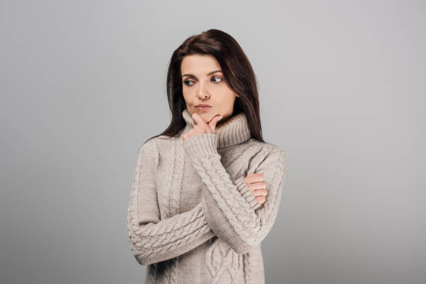 istock pensive woman in cozy sweater isolated on grey 1185686744