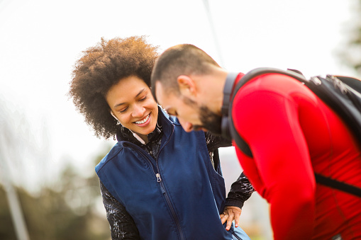Young athletic woman talking to her partner while standing on a jogging track in a city park.