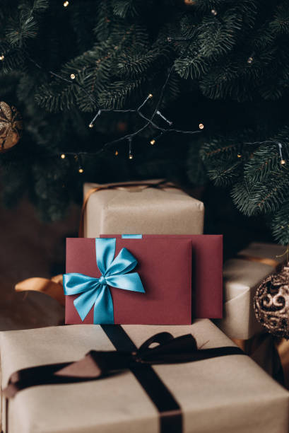 istock Gift voucher in burgundy envelope with blue bow under the Christmas tree. Christmas gift 1185708770