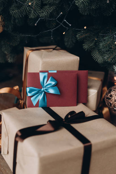 istock Gift voucher in burgundy envelope with blue bow under the Christmas tree. Christmas gift 1185708866