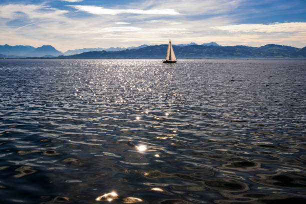 Sailboat on glittering water, blue mountains in horizon in sunny day. Lake Constance, Europe.