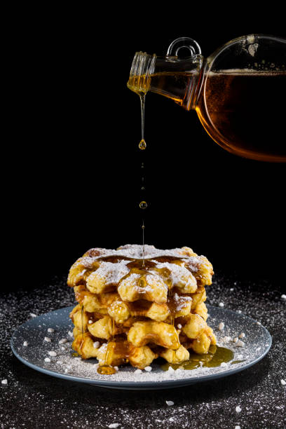 Fresh crispy Belgian waffles tower with icing sugar and crunchy sugar crystals. Maple syrup pouring from bottle above. stock photo