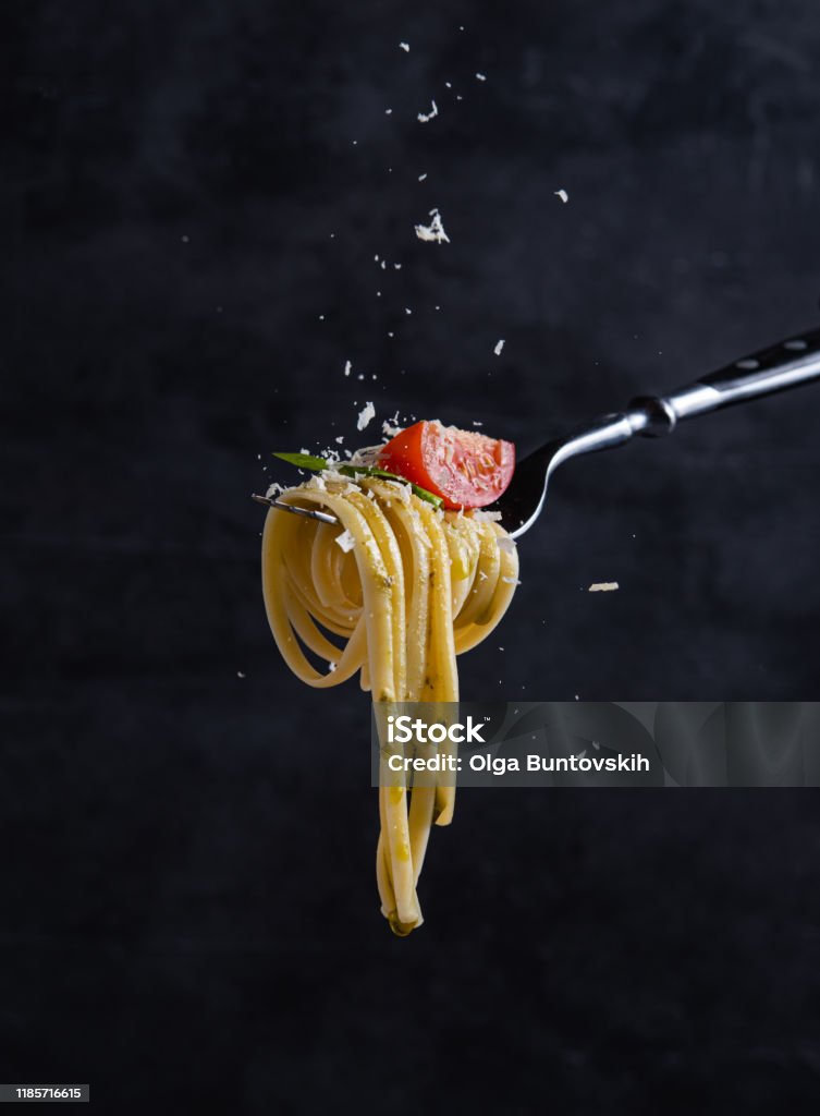 tagliatelle con tomate y pesto en el tenedor. Comida italiana. Fondo oscuro - Foto de stock de Pasta libre de derechos
