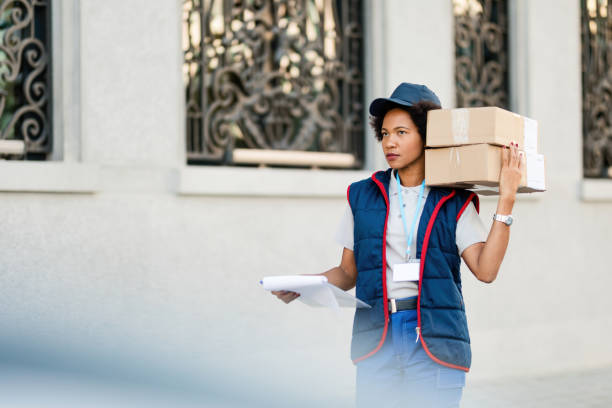 istock Black female courier delivering packages while walking down the street. 1185724876