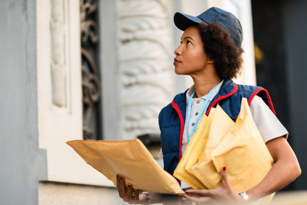 African American postal worker delivering mail in the city. Black postwoman delivering mail in residential district. home delivery photos stock pictures, royalty-free photos & images