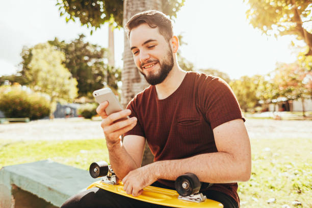 junger skater-mann mit smartphone im park - skateboard skateboarding outdoors sports equipment stock-fotos und bilder