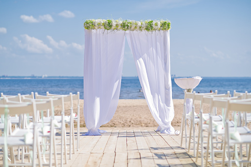 White wedding arch decorated with flowers on the shore of the blue sea. Wedding celebration, the wedding ceremony of the bride and groom