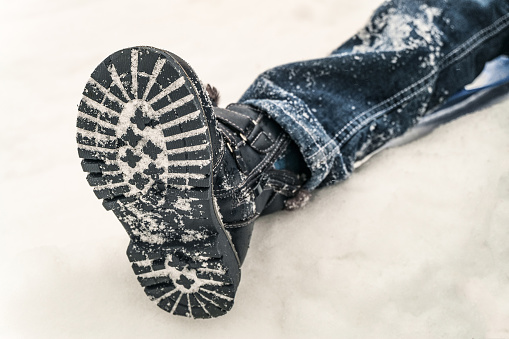Winter non-slip shoes on the feet of a boy lying in the snow. Child boot.