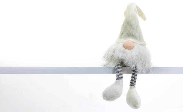 Gnome a Christmas elf is relaxed and sitting on white shelf with hanging legs Gnome a Christmas elf is relaxed and sitting on white shelf with hanging legs elf sitting stock pictures, royalty-free photos & images